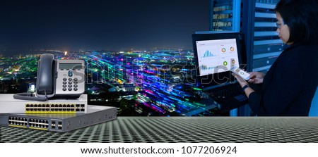 IP Telephone and Network switch 24 port gigabit and System administrator working in data center and blending with smart city at night for high speed telecommunication.