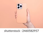 iPhone 15 pro in female hand in fuzz peach silicone cover isolated on 2024 pantone color of the year background phone case mock up in monochrome colours back view