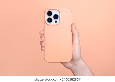 iPhone 15 pro in female hand in fuzz peach silicone cover isolated on 2024 pantone color of the year background phone case mock up in monochrome colours back view