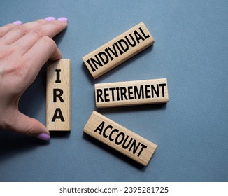 IRA - Individual Retirement Account symbol. Concept word IRA on wooden blocks. Businessman hand. Beautiful grey background. Business and IRA concept. Copy space.