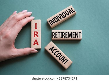 IRA - Individual Retirement Account symbol. Concept word IRA on wooden blocks. Businessman hand. Beautiful grey green background. Business and IRA concept. Copy space.
