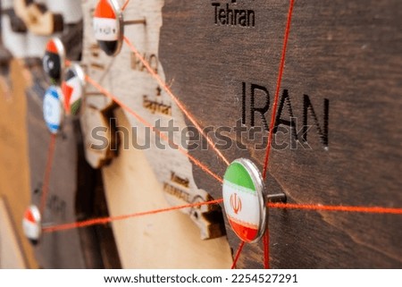 Iran flag on the pushpin with red thread showed the paths of movement or areas of influence in the global economy on the wooden map. Planning of traveling or logistic concept. Networks connection