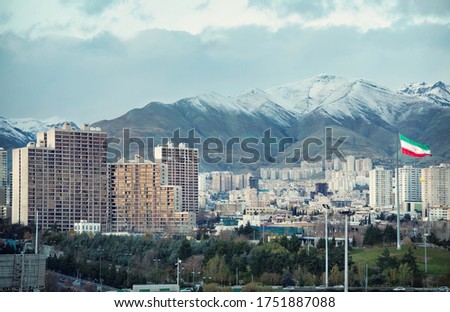 Iran flag and Tehran City skyline against snow covered Alborz Mountains