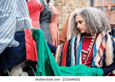 Iranian Mature Woman Shopping Outfits In A Street Market Shop. There Are Manikins With Clothes And She Is Watching A Green Dress.