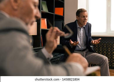 Irascible Man. Unbalanced Angry Married Man Gesticulating While Sitting In The Psychotherapists Office And Looking Into The Distance