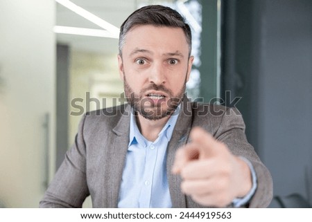 An irate businessman pointing a finger while talking angrily on a video call, showing frustration and aggression.