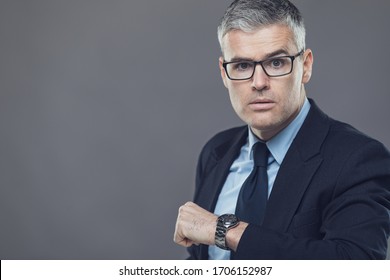 Irate Manager Or Boss Glaring At A Latecomer For A Meeting Holding Up His Wristwatch With A Stern Unimpressed Expression Isolated On Grey