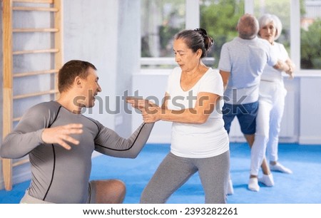 Irate mature female trainee applying armlock technique on person in sports hall