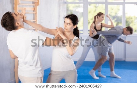Irate young female attendee of self-defense classes fighting with male opponent in sports hall