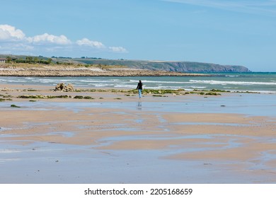 Ireland 2022-08-31  Lone Female Figure Walking On The Beach At Ardmore, County Waterford At Low Tide.