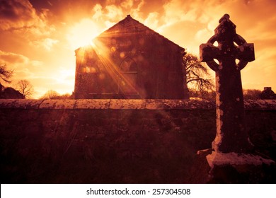 Ireland celtic cross at medieval church cemetery under fiery sky