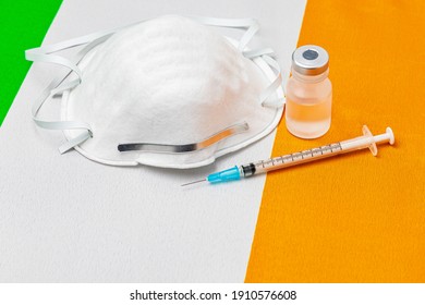 Ireland Flag, N95 Face Mask, Needle Syringe And Vial. Concept Of Covid-19 Coronavirus Vaccine Distribution, Supply Shortage And Healthcare Crisis