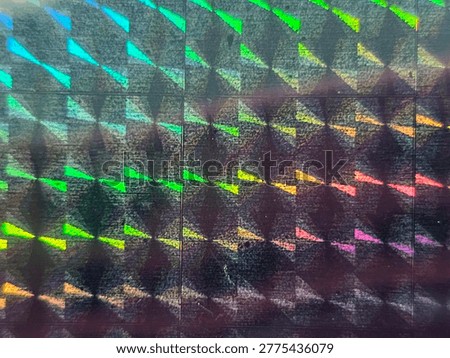 Iridescent geometric surface with diamond and triangular segments reflecting rainbow hues of blue, green, yellow, orange, and pink, forming vivid holographic abstract texture across panels.