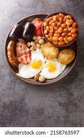 Irish Breakfast With Fried Egg, Sausages, Black Pudding, Baked Beans, Bacon, Tomato, Hash Browns And Grilled Mushrooms Closeup In The Plate On The Table. Vertical Top View From Above
