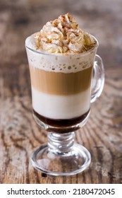 Irish coffee with whipped cream, cocoa powder, chocolate syrup and whiskey. Drink in a glass, transparent glass with a handle, on a stem. The glass stands on a rustic background.