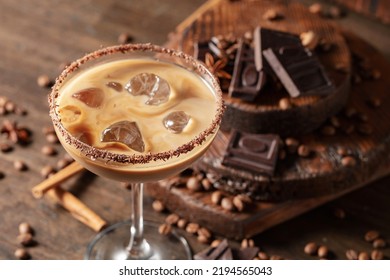 Irish cream and coffee cocktail in a glass with ice on an old wooden background. Coffee beans, cinnamon, anise, and pieces of chocolate are scattered on the table. 
