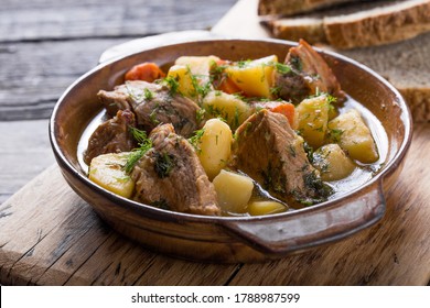 Irish dinner. Beef meat stewed with potatoes, carrots and soda bread on wooden background, top view, copy space. Homemade winter comfort food - slow cooked