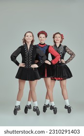 Irish ensemble of three beautiful women in concert costumes and Ghillies Hard Shoes dance together in a row. Full-length studio portrait on a grey background. - Shutterstock ID 2310291403