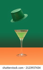 Irish festival minimal concept. Martini glass with green cocktail on terracotta table. Green glitter hats levitate above on a dark green background.