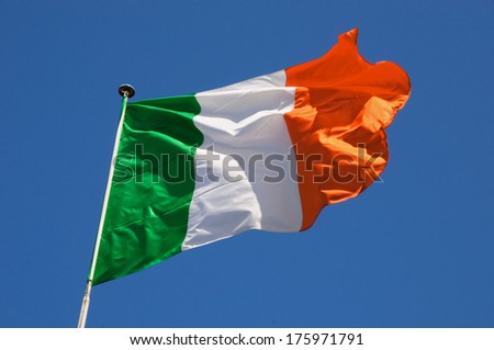 Irish flag fluttering in a brisk breeze against a bright blue sky.