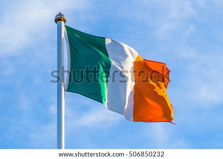 Irish flag waving in the wind in the early morning at sunrise against a blue cloudy sky