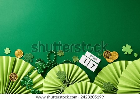 Irish jigs and jollity: St. Patrick's Day merriment. Side view photo of cube calendar, folding fans, trefoils, coins, beads on green background with space for greetings