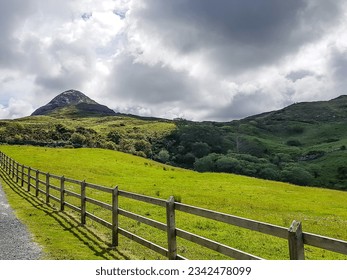 Irish landscape of Connemara national park, mountains with trees and green grass, Diamond Hill against gray stormy sky in background, pedestrian path next to a wooden fence in Letterfrack, Ireland - Powered by Shutterstock