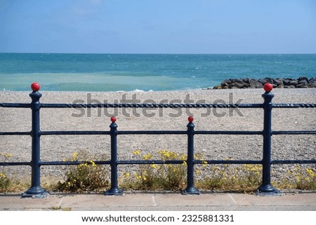 The Irish Sea and pebble beach seen through symmetrical metal railings of the promenade in Bray, Ireland.