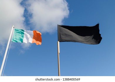 Irish Tricolour And Black Flag Flying Against A Blue Sky