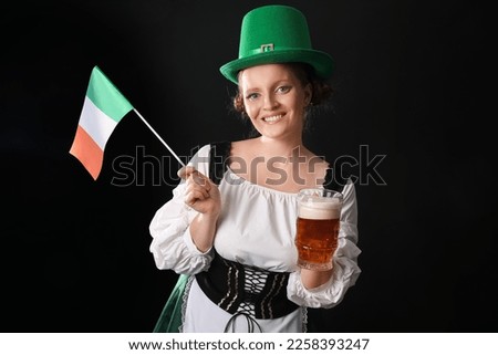 Irish waitress with beer and flag of Ireland on dark background. St. Patrick's Day celebration