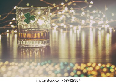 Irish Whiskey St Patricks Clover Golden Glow. Irish whiskey in a glass with a clover symbol, on a pub table with gold beads and bar lights. - Powered by Shutterstock