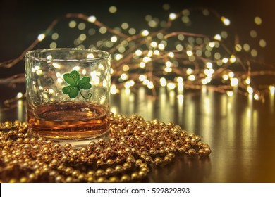 Irish Whiskey St Patricks Clover. Irish whiskey in a glass with a clover symbol, on a pub table with gold beads and bar lights. - Powered by Shutterstock