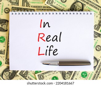 IRL In Real Life Symbol. Concept Words IRL In Real Life On White Note On A Beautiful Background From Dollar Bills. Metallic Pen. Business And IRL In Real Life Concept. Copy Space.