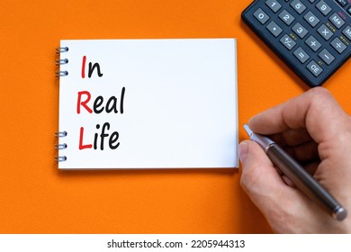 IRL In Real Life Symbol. Concept Words IRL In Real Life On White Note On A Beautiful Orange Background. Businessman Hand. Black Calculator. Business And IRL In Real Life Concept. Copy Space.