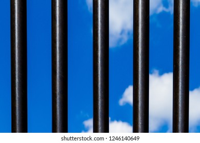 Iron bars in front of blue sky with clouds, steel bars isolated with blue sky view, creates the impression of prison or jail bars
