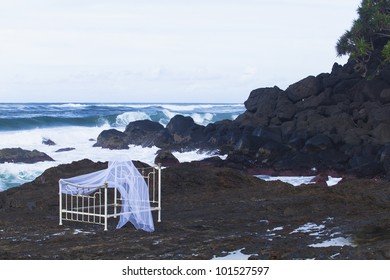 Iron Bed Frame And Mosquito Net On Beach Rocks