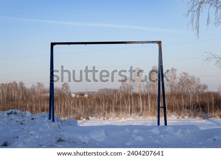An iron black rack for summer swings on a snow-covered playground. Without a swing