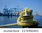 A iron bollard with a tied rope on a quay in the Port of Rotterdam in the Netherlands. In the background, slightly out of focus, is the industrial area of the Maasvlakte near Rotterdam.