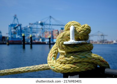 A iron bollard with a tied rope on a quay in the Port of Rotterdam in the Netherlands. In the background, slightly out of focus, is the industrial area of the Maasvlakte near Rotterdam.