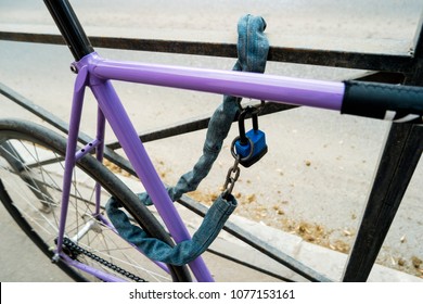 Iron Chain And Lock On A Old Bicycle Of Violet Color. Locked Bicycle At Bicycle Outdoor Parking Space