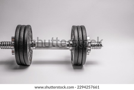 Iron dumbbell with black discs on a light background.