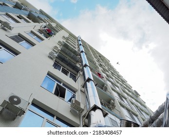 Iron Exhaust Pipe On The Apartment Building. Maintenance Of Apartment Buildings. Facade Of A High-rise Residential Building Against A Cloudy Sky. Bottom Up Perspective View