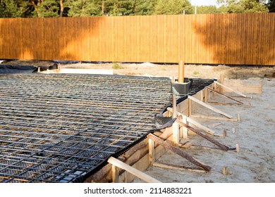 Iron fittings on a wooden formwork with laid pipes are the basis for pouring the foundation of the house with a concrete slab. Construction of cottages, design, engineering communications. - Shutterstock ID 2114883221