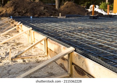 Iron fittings on a wooden formwork with laid pipes are the basis for pouring the foundation of the house with a concrete slab. Construction of cottages, design, engineering communications.