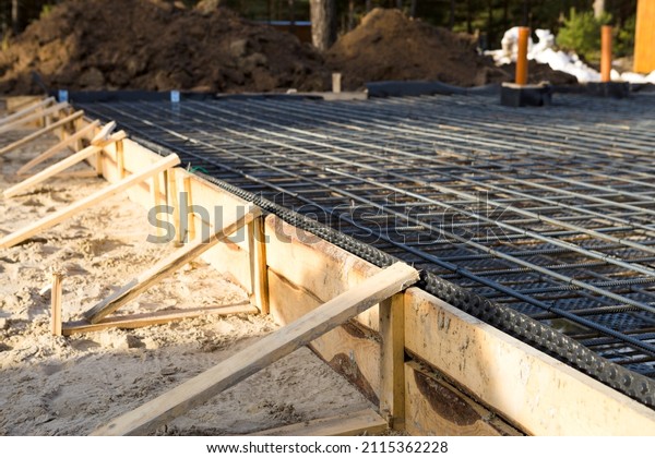 Iron fittings on a wooden formwork with
laid pipes are the basis for pouring the foundation of the house
with a concrete slab. Construction of cottages, design, engineering
communications.