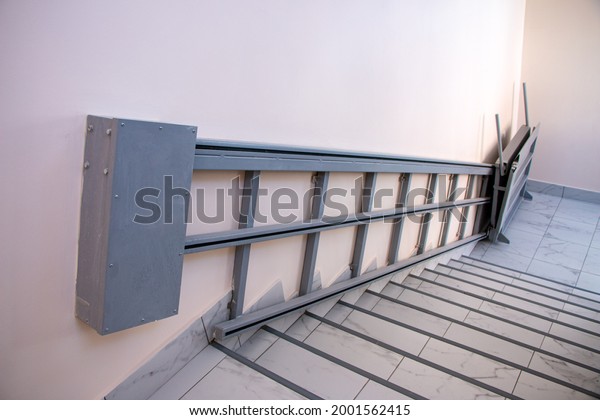 iron gray electric wheelchair lift with a ramp and\
a chain mechanism for lifting along the stairs, for lifting\
wheelchairs to the floor\
above.