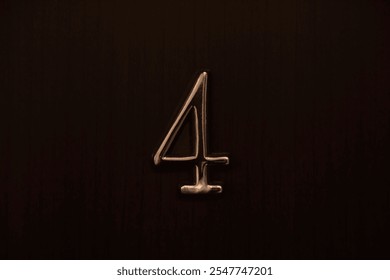 iron House number 4 on a brown wooden front door. flat room apartment in hotel metal digit four on grey wood wall fence with black door. screwed down with a screw. in front view.