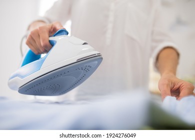 Iron, ironing. Female thin hands holding modern iron with quality sole over white cloth, positive