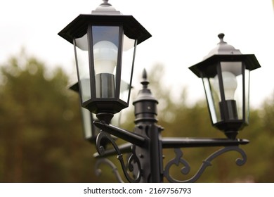 An iron lantern stands and illuminates the road in the village. Road lighting, light bulbs in a lamppost