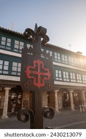 Iron made Emblem of the Order of Calatrava iluminated by the morning sun. red Greek cross with fleur-de-lis at its ends, in the Plaza Mayor of Almagro, Ciudad Real. Bokeh in the background. Trav